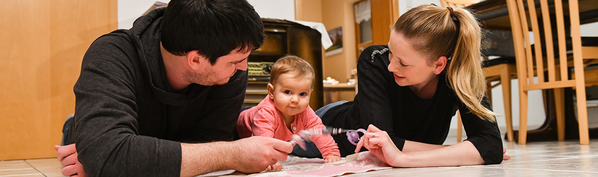 Junge Eltern spielen auf dem Boden liegend mit ihrem Baby